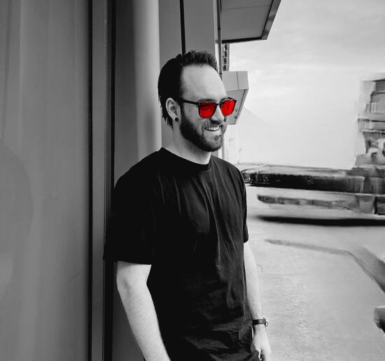 an image of Bruce Hollows, with sunglasses on leaning on wall of a building, black and white photo with red sunglasses lens